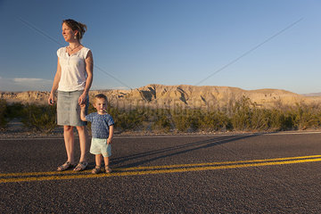 Mother and toddler son walking together on paved road through desert