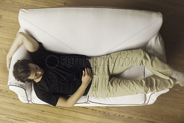 Man reclining on couch listening to music playing on smartphone