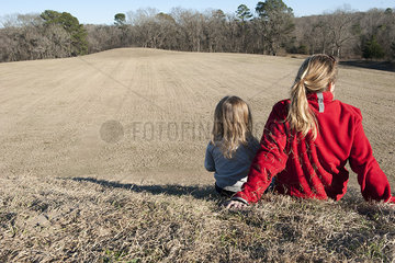 Mother and daughter sitting together on hill  rear view