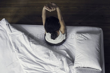 Woman sitting on edge of bed stretching
