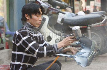 Ein Mann lackiert eine Mopedkarosserie auf dem Gehweg