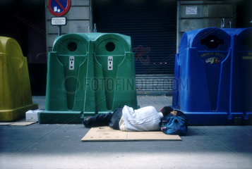 Neben Containern schlaeft ein Mensch auf dem Boden in Barcelona