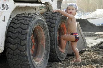 Pajara  ein Kleinkind klettert auf den Reifen eines Baggers