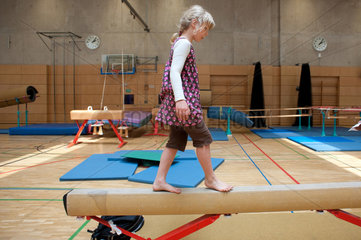 Berlin  Deutschland  blondes Maedchen balanciert auf einem Schwebebalken in einer Turnhalle