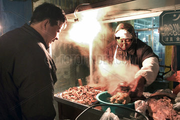 Peking  Haendlerin auf einem Markt bereitet Fleisch zu