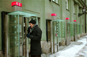 Mann telefoniert mit oeffentlichem Telefon im Winter