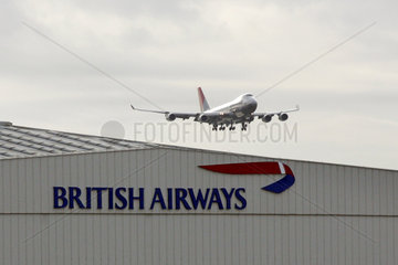 London  ein Passagierflugzeug fliegt ueber einen Hangar der British Airways