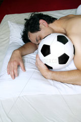 Berlin  Deutschland  Mann liegt mit Fussball im Bett