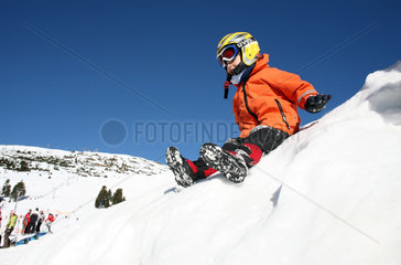 Jerzens  Oesterreich  ein Kind mit Helm rutscht einen schneebedeckten Hang herunter