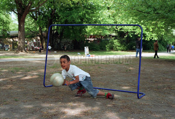 Sproessling einer Einwandererfamilie spielt Fussball im Park in Berlin-Kreuzberg