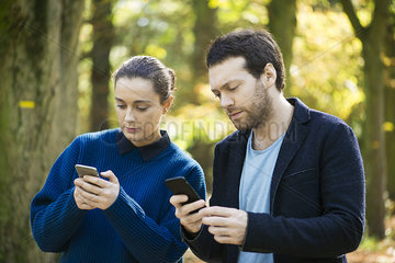 Couple checking smartphones while walking in woods