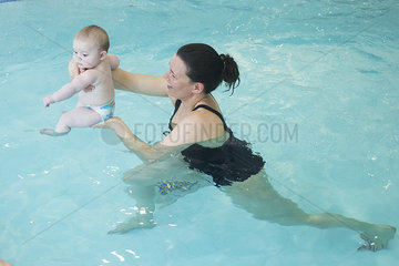 Mother in swimming pool holding infant at water's surface