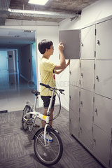 College student pausing by lockers with bicycle