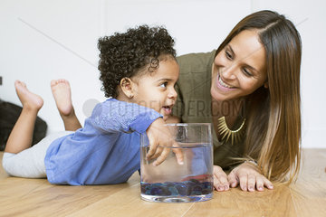 Mother and toddler daughter playing with pet goldfish