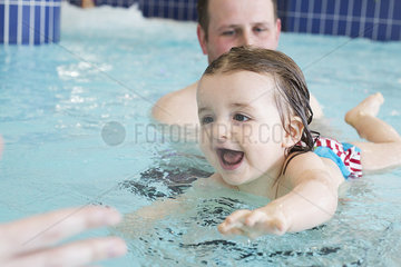 Little girl learning to swim with help of parent