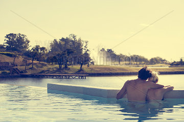Couple relaxing in infinity pool overlooking lake