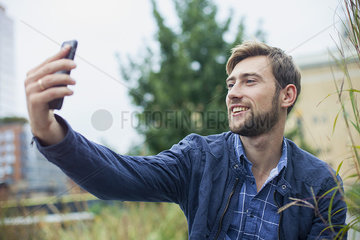 Young man using smartphone to take a selfie outdoors