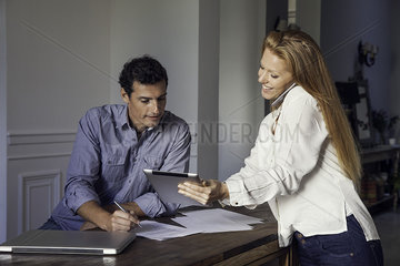 Woman talking on cell phone and showing husband digital tablet