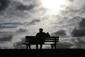 Hannover  alter Mann sitzt vor dramatischem Wolkenhimmel lesend auf einer Bank