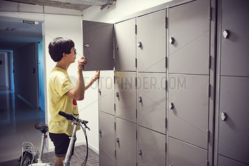 College student opening locker in corridor