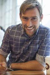 Man sitting in coffee shop with credit card in hand  smiling cheerfully