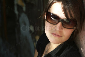 Berlin  junge Frau mit Sonnenbrille lehnt an einer Mauer