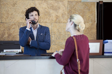 Impatient customer waiting while hotel receptionist talks on phone