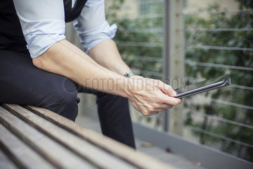 Man sitting on bench  using digital tablet  cropped