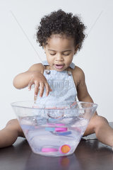 Toddler girl playing with toys in bowl of water