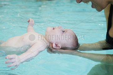 Mother teaching infant how to float in swimming pool