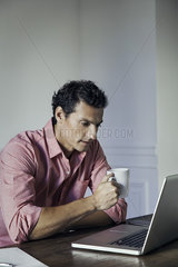 Man drinking coffee while using laptop computer