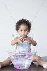 Toddler girl playing with toys in bowl of water