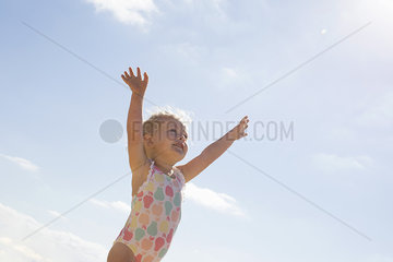 Little girl standing on beach with arms raised