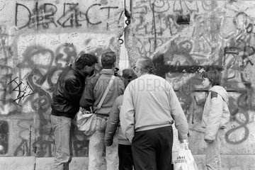Berlin  Deutschland  Maenner schauen durch ein Loch in der Mauer auf den Grenzstreifen