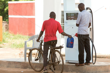 Kamdini  Uganda - Strassenszene. Ein Fahrradfahrer laesst sich an einer Zapfsaeule einer Tankstelle seinen Plastikkanister mit Treibstoff auffuellen.