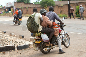 Kamdini  Uganda - Strassenszene mit Menschen und Motorraedern. Drei Maenner fahren auf einem Motorrad.