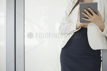Woman leaning against wall  using digital tablet  cropped