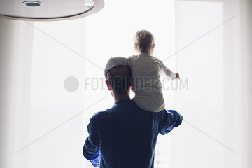 Father carrying son on shoulder  looking out of window together