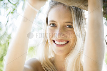 Young woman leaning against tree branch  smiling  portrait