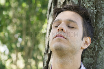 Man leaning against tree lost in thought