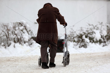 Berlin  Deutschland  Seniorin mit Rollator laeuft einen schneebedeckten Gehweg entlang