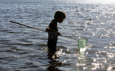 Wusterhausen  Deutschland  Junge steht mit einem Kescher im Wasser in einem See