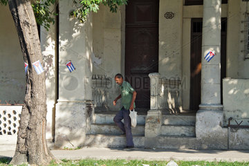 Havanna  Kuba  ein Mann verlaesst altes Haus  um ihn herum aufgeklebte Nationalfahnen