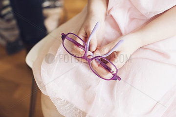 Girl holding pair of glasses on lap  cropped
