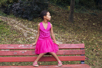 Girl sitting alone on park bench  looking away in thought