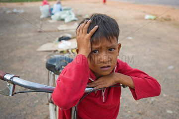Kampot  Kambodscha  ein Junge lehnt ueber den Lenker seines Fahrrades am Strassenrand