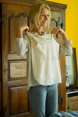 Mature woman standing in bedroom  holding blouse against her chest and smiling