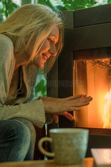 Mature woman warming her hands by fireplace
