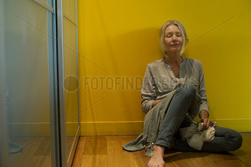 Mature woman sitting on floor with clothes in hands  eyes closed