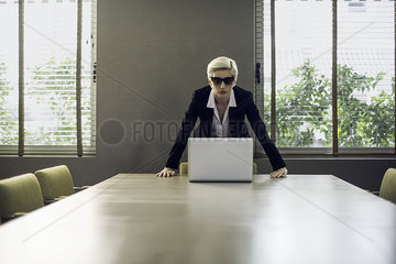 Woman in suit leaning against table looking at camera